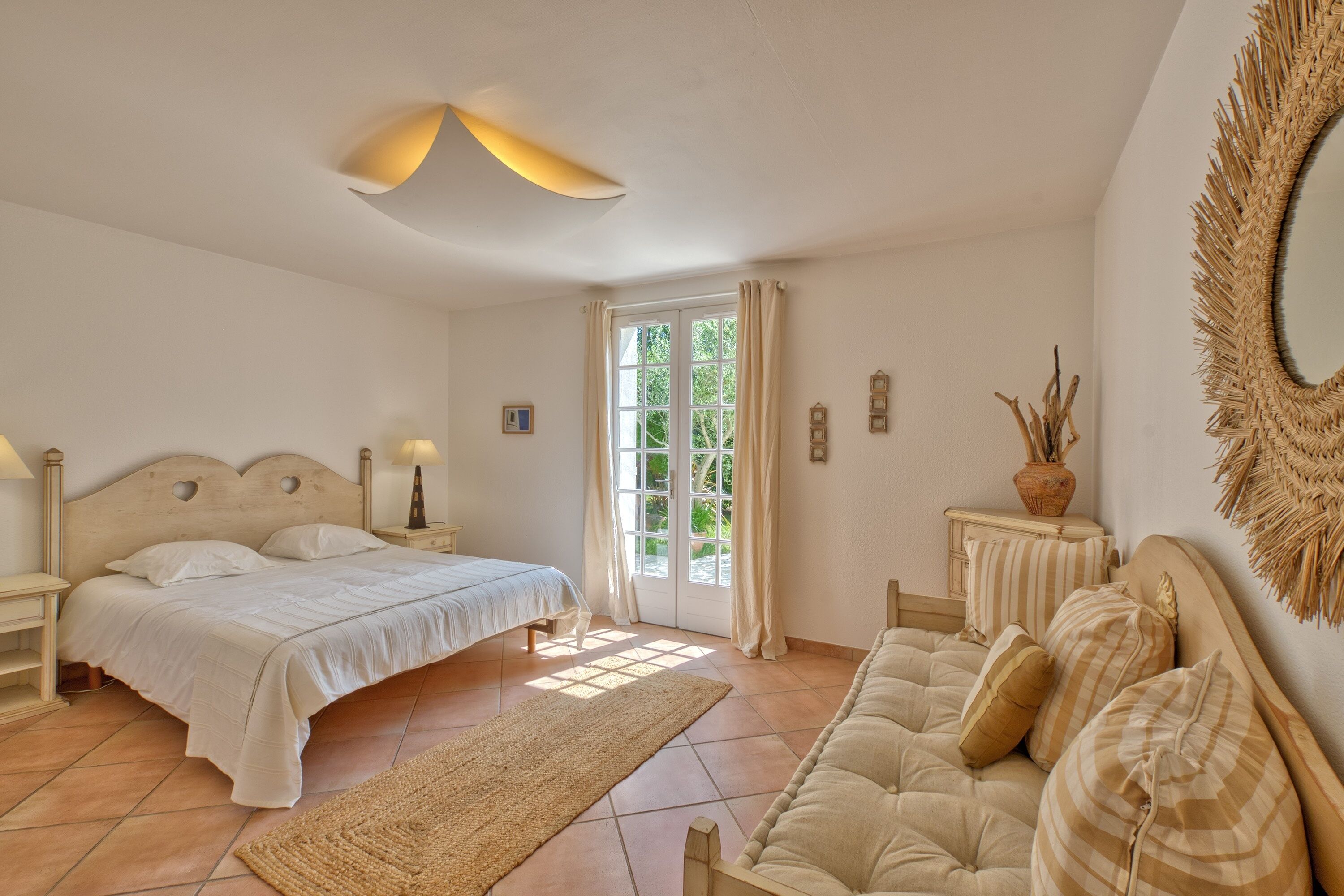 A bedroom with a bed, a sofa, a nightstand, a lamp, a mirror, and a door leading to a balcony.