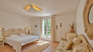 A bedroom with a bed, a sofa, a nightstand, a lamp, a mirror, and a door leading to a balcony. - Le Temps des Vacances - À 500 m de la plage (La Brée-les-Bains)