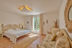 Ein Schlafzimmer mit einem Bett, einem Sofa, einem Nachttisch, einer Lampe, einem Spiegel und einer Tür, die auf einen Balkon führt.