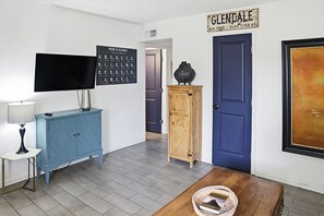 Une piĂšce Ă©quipĂ©e dâun tĂ©lĂ©viseur Ă Ă©cran plat, dâune affiche prĂ©sentant lâalphabet phonĂ©tique, dâune armoire en bois, dâune porte bleue et dâune Ćuvre dâart encadrĂ©e.