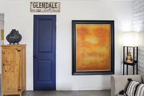 A blue door, a framed abstract painting, a wooden cabinet, and a lamp on a brick wall. - 2-Bedroom in Glendale near Westgate and Stadium with AC, Pet Friendly! (Glendale)