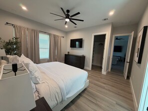 Una camera da letto con un letto, un ventilatore a soffitto, una TV, una cassettiera e un armadio a muro.