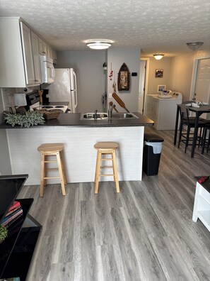 Une cuisine moderne avec des meubles blancs, un îlot central doté de tabourets, un lave-linge et un coin repas avec une table et des chaises.