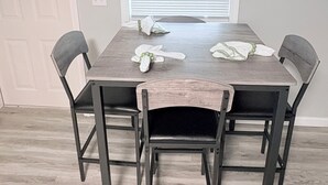 A dining table with four chairs, a window with blinds, a door, and a wall-mounted light switch. - Lovely 2-bedroom mobile home with AC in Corbin. Only .4 miles from Laurel Lake. (Corbin)