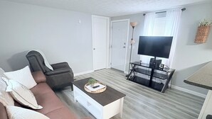 A living room with a brown sofa, a white coffee table, a TV, and a dining area with a table and chairs. - Lovely 2-bedroom mobile home with AC in Corbin. Only .4 miles from Laurel Lake. (Corbin)
