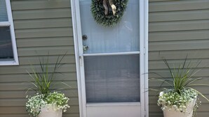 A house with a grey exterior, a white front door with a wreath, and two potted plants on either side of the door. - Lovely 2-bedroom mobile home with AC in Corbin. Only .4 miles from Laurel Lake. (Corbin)