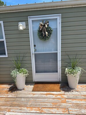A house with a grey exterior, a white front door with a wreath, and two potted plants on either side of the door.