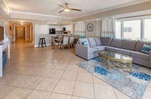 A spacious living area with a sofa, coffee table, and dining table. A kitchen is visible in the background. - Spacious 2-bedroom beachfront condo in Orange Beach with private jacuzzi tubs (Orange Beach)