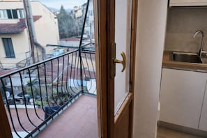 Ein Balkon mit Metallgeländer, Blick auf Gebäude und eine Küchenzeile mit Spüle.