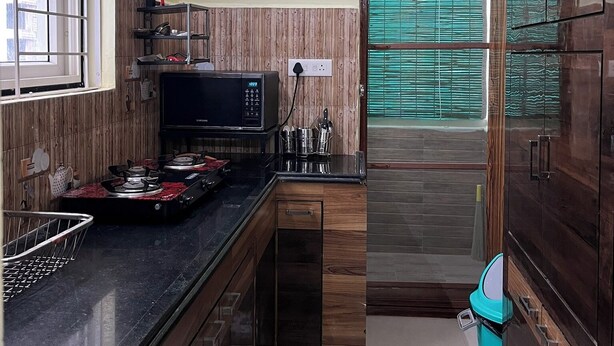 A compact kitchen with a microwave, gas stove, and wooden cabinets. - Premium 1BHK Gachibowli -Walk to AIG (Hyderabad)