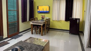 A living room with a dining table, chairs, a sofa, a TV mounted on the wall, and a refrigerator. - Premium 1BHK Gachibowli -Walk to AIG (Hyderabad)