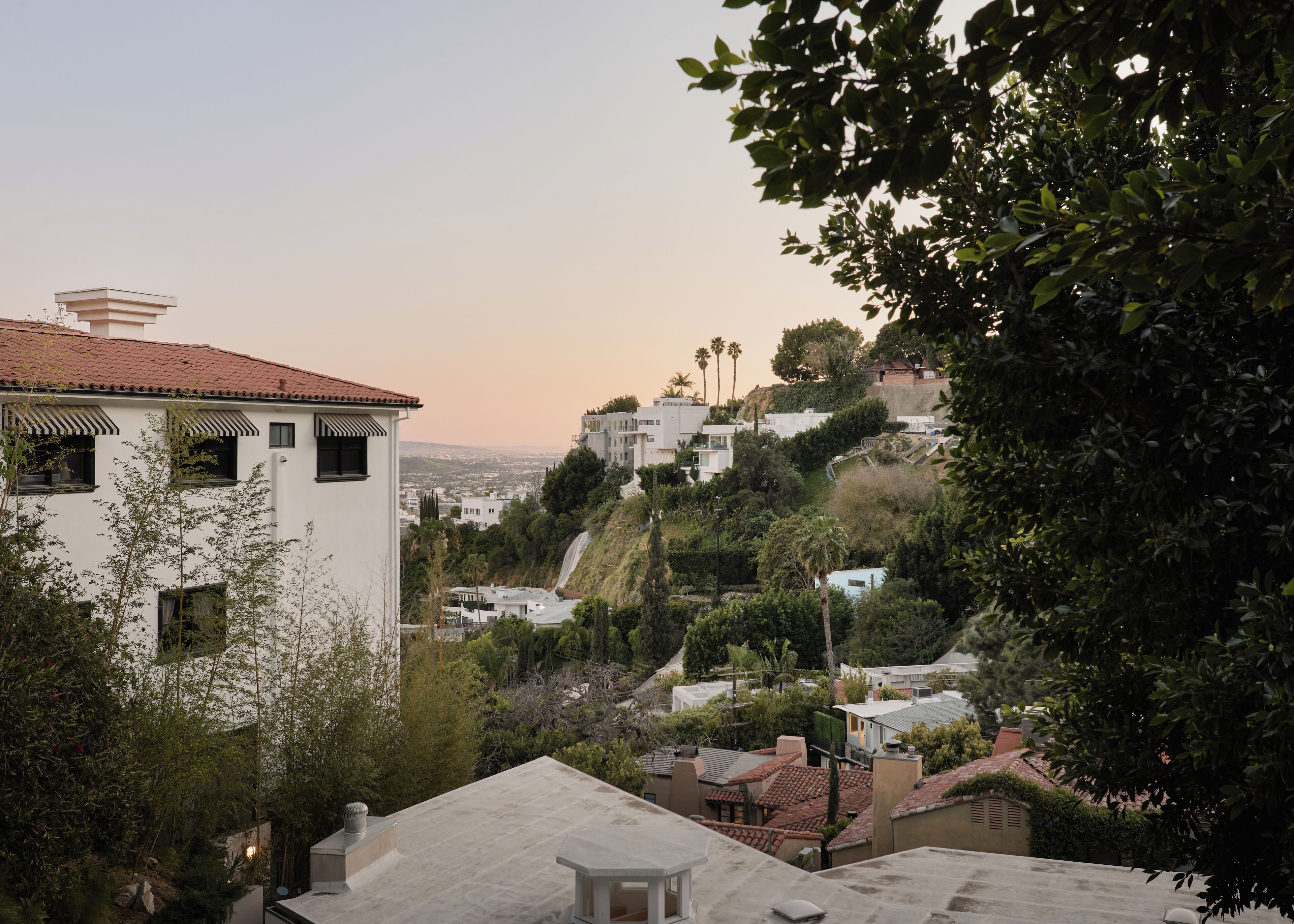 A residential area with houses on a hillside, including a white house with a red-tiled roof and a modern building with a sloped roof.