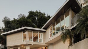 Ein modernes, zweistöckiges Haus mit Balkon, einer Treppe zum Eingang und einem angelegten Garten.