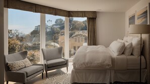 Ein Schlafzimmer mit großem Fenster, einem Bett, zwei Sesseln und einem gemusterten Teppich.