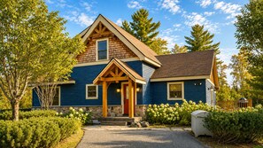 Une maison à deux étages, avec des fondations en pierre, un porche en bois et une porte rouge.