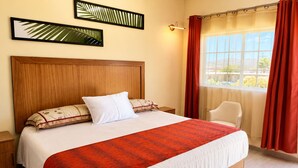Una habitación de hotel con una cama grande, un cabecero de madera, una mesita de noche, una silla y una ventana con cortinas.