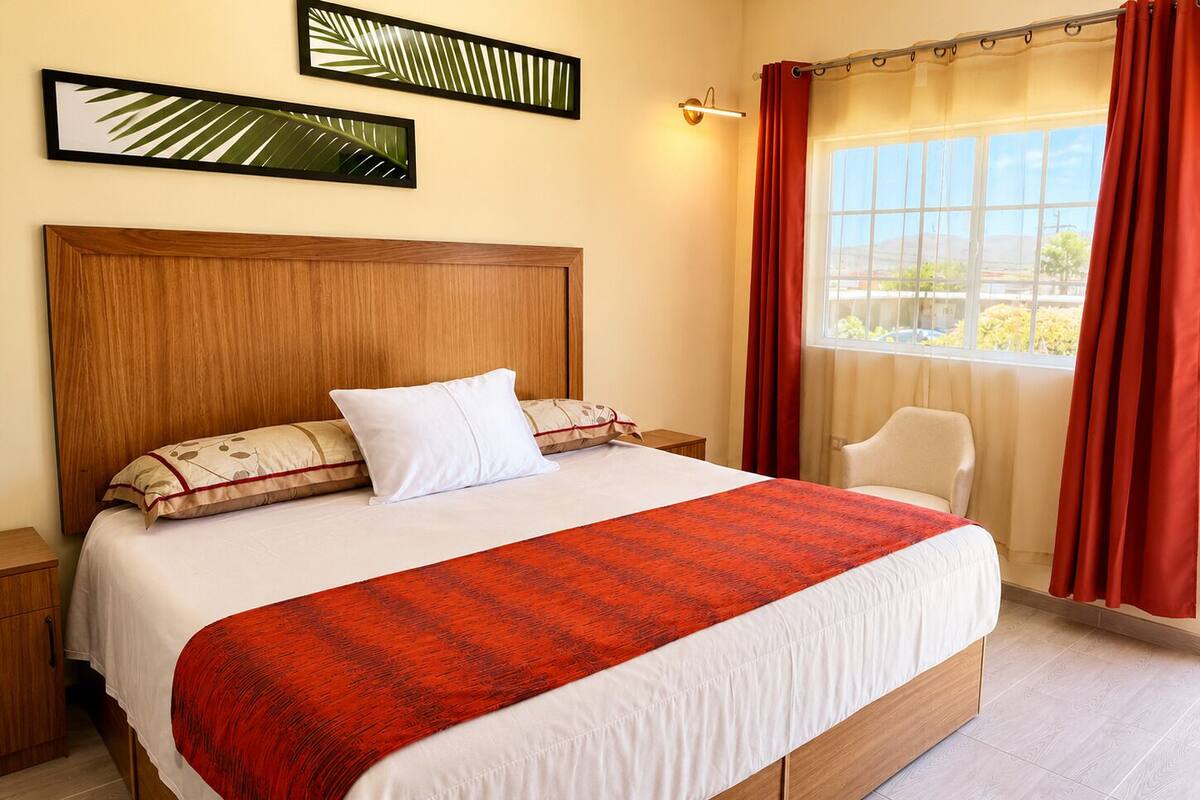 A hotel room with a large bed, a wooden headboard, a nightstand, a chair, and a window with curtains.