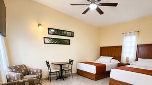 Una habitación de hotel con ventilador de techo, dos camas, un sofá, una mesa y una silla.