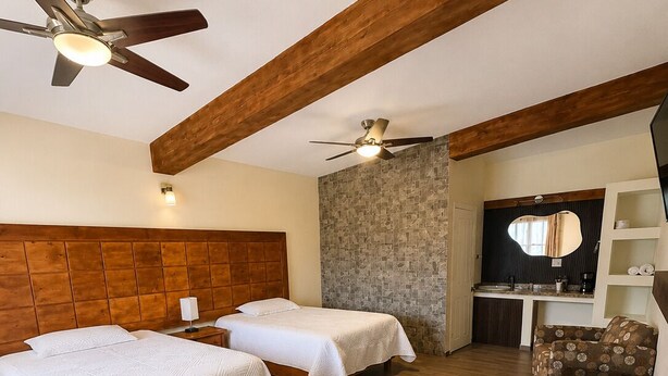 Habitación de hotel con dos camas, techo de madera, pared de acento de piedra, un escritorio pequeño, una silla y un ventilador de techo.