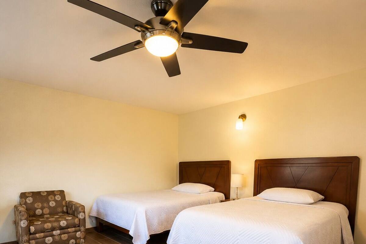 A hotel room with two beds, a ceiling fan, a chair, and a nightstand.