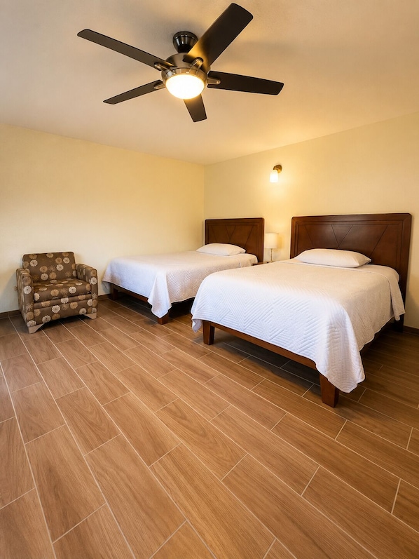 A hotel room with two beds, a ceiling fan, a chair, and a nightstand.