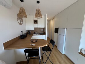 A compact kitchen with a wooden island, two black chairs, a small table, and a hanging light fixture. - Tiny House de Romy, 4 personnes, pieds dans l'eau (Le Cap d'Agde)