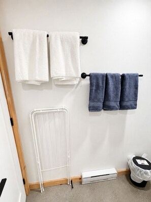 A bathroom with two towel racks, one with white towels and one with blue towels, a white radiator, and a white air conditioning unit. - Lakeside Cabin Retreat with Beach, Kayaks, Fire Pit & Forest Trails (Sainte-Marguerite-du-Lac-Masson)