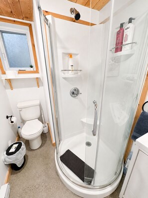 Et moderne badeværelse med et glasafskærmet brusebad, toilet og et lille vindue.