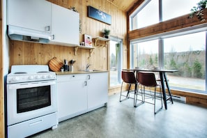 Een keuken met een fornuis, kastjes, een raam en een tafel met stoelen.