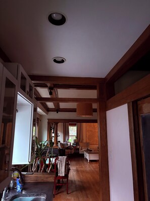 Ein Zimmer mit Holzbalken, einer Küchenzeile inklusive Spüle sowie einem Essbereich mit Stuhl und Tisch.
