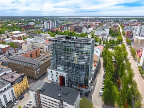 Un área urbana moderna con un edificio de cristal destacado, rodeado de otros edificios y un cielo despejado.