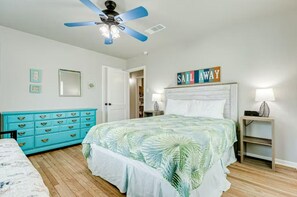 Ein Schlafzimmer mit Bett, Deckenventilator, Kommode, Nachttisch und Wandregal.