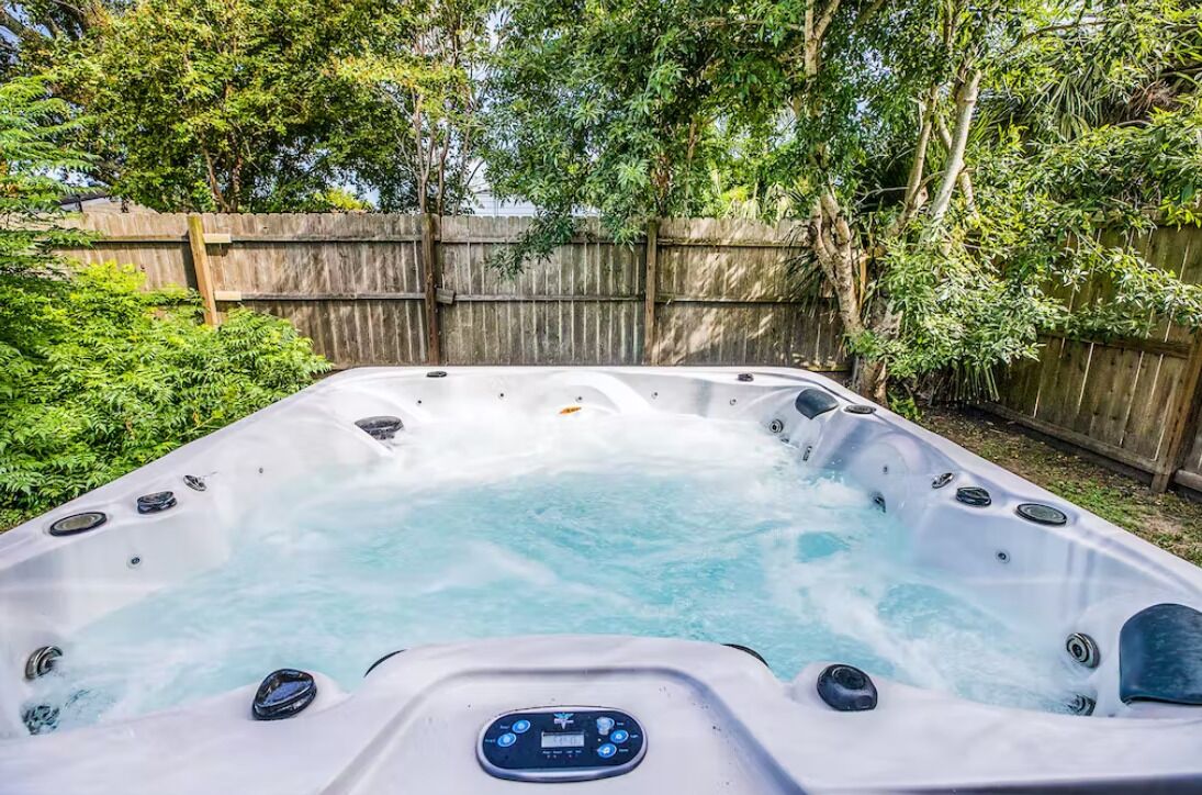 Un jacuzzi con panel de control, rodeado de una valla de madera y follaje.