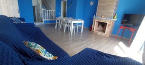 A living room with a blue sofa, a fireplace, a TV, and a dining area with white chairs. - Villa María - Beautiful beachfront villa with private pool in Vinaròs - Ref 856 (Vinaròs)