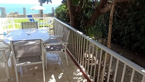 Een terras met een ronde tafel en stoelen, een witte balustrade en uitzicht op zee.