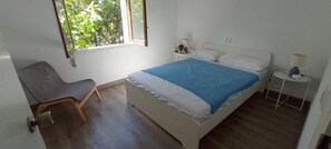 A bedroom with a bed, a chair, a bedside table, a lamp, and a window with a view of greenery. - Villa María - Beautiful beachfront villa with private pool in Vinaròs - Ref 856 (Vinaròs)