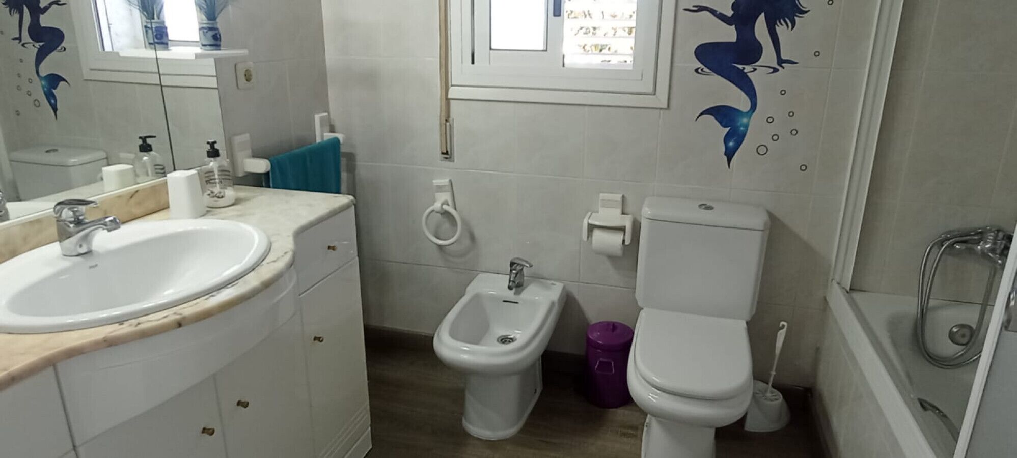 A bathroom with a sink, bidet, toilet, and a window with a view.