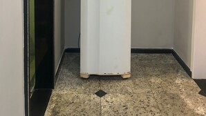 Een witte koelkast in een hal met een deur aan de linkerkant en een lamp aan het plafond.