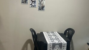 Een eetruimte met een tafel bedekt met een kantkleed, omringd door zwarte stoelen, en drie ingelijste kunstwerken aan de muur.