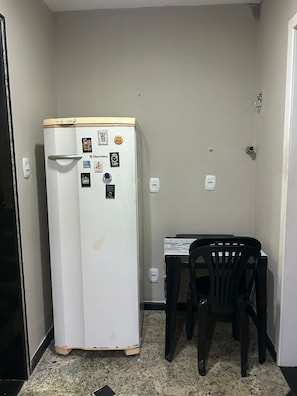 Una cuina americana petita amb un frigorífic blanc, una taula amb una cadira i una porta.