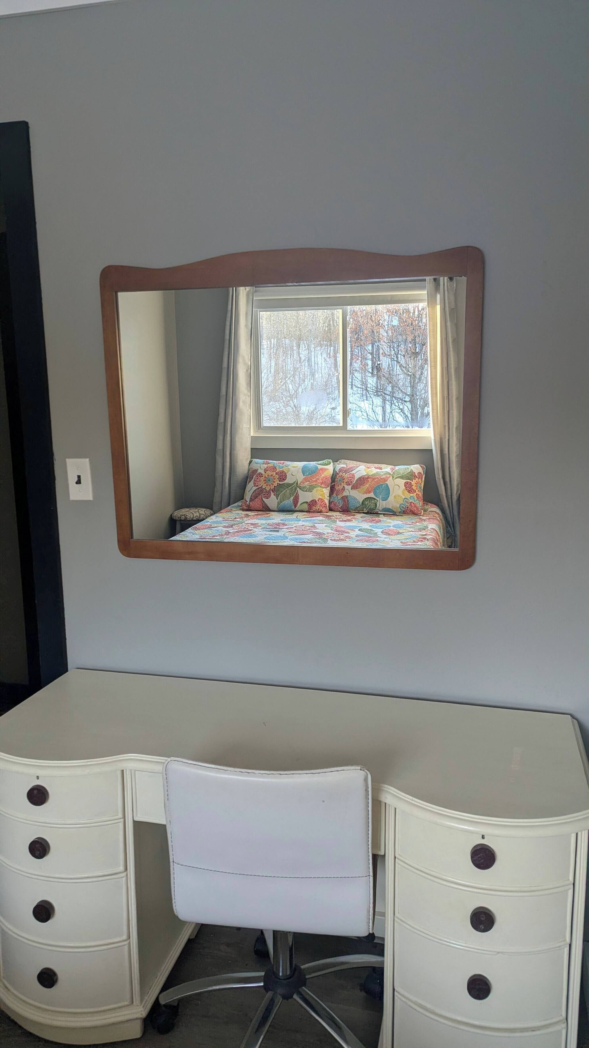 A bedroom with a bed, a dresser, a chair, and a large mirror.