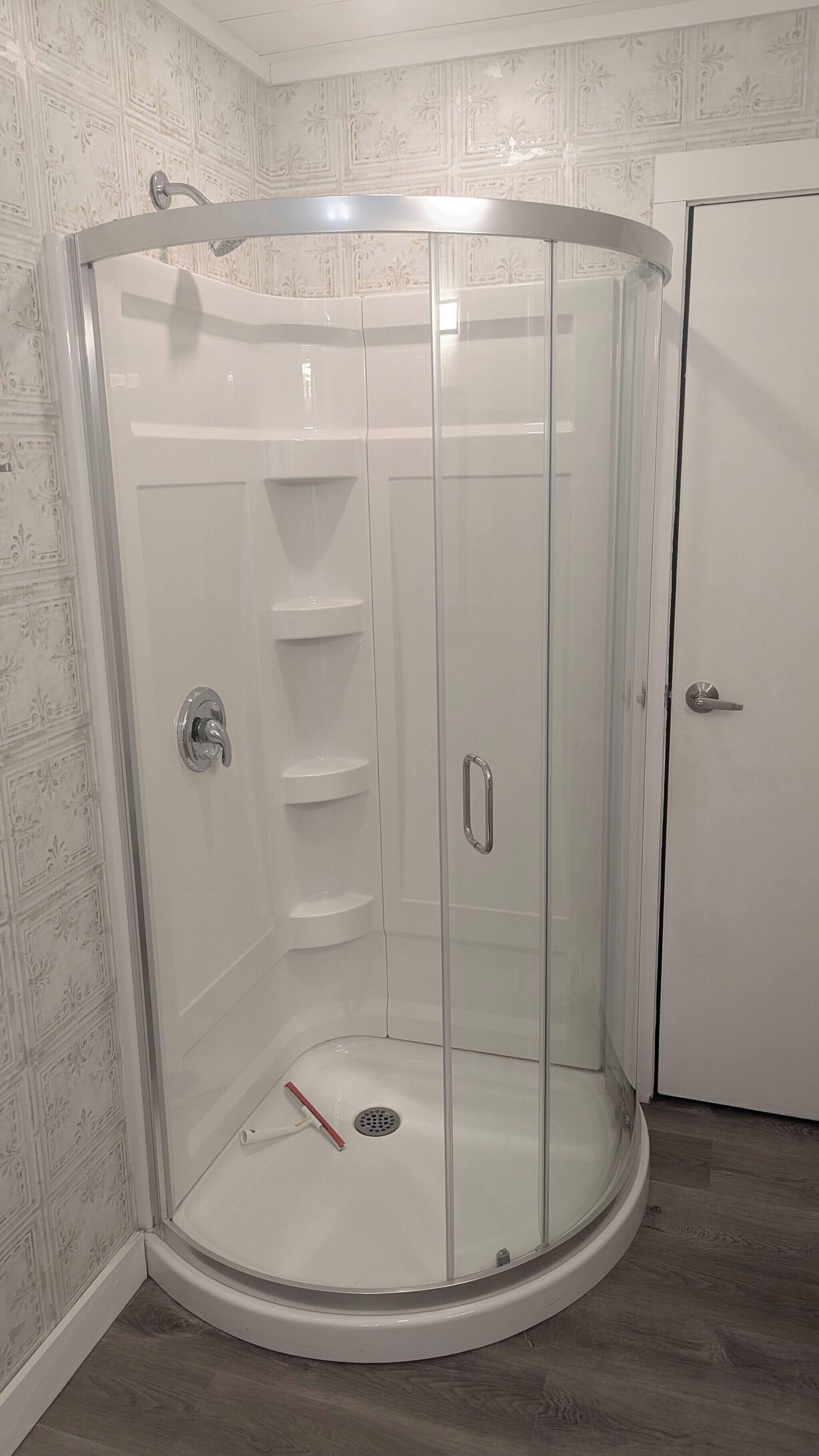 A glass-enclosed shower stall with a showerhead, a door handle, and a drain.