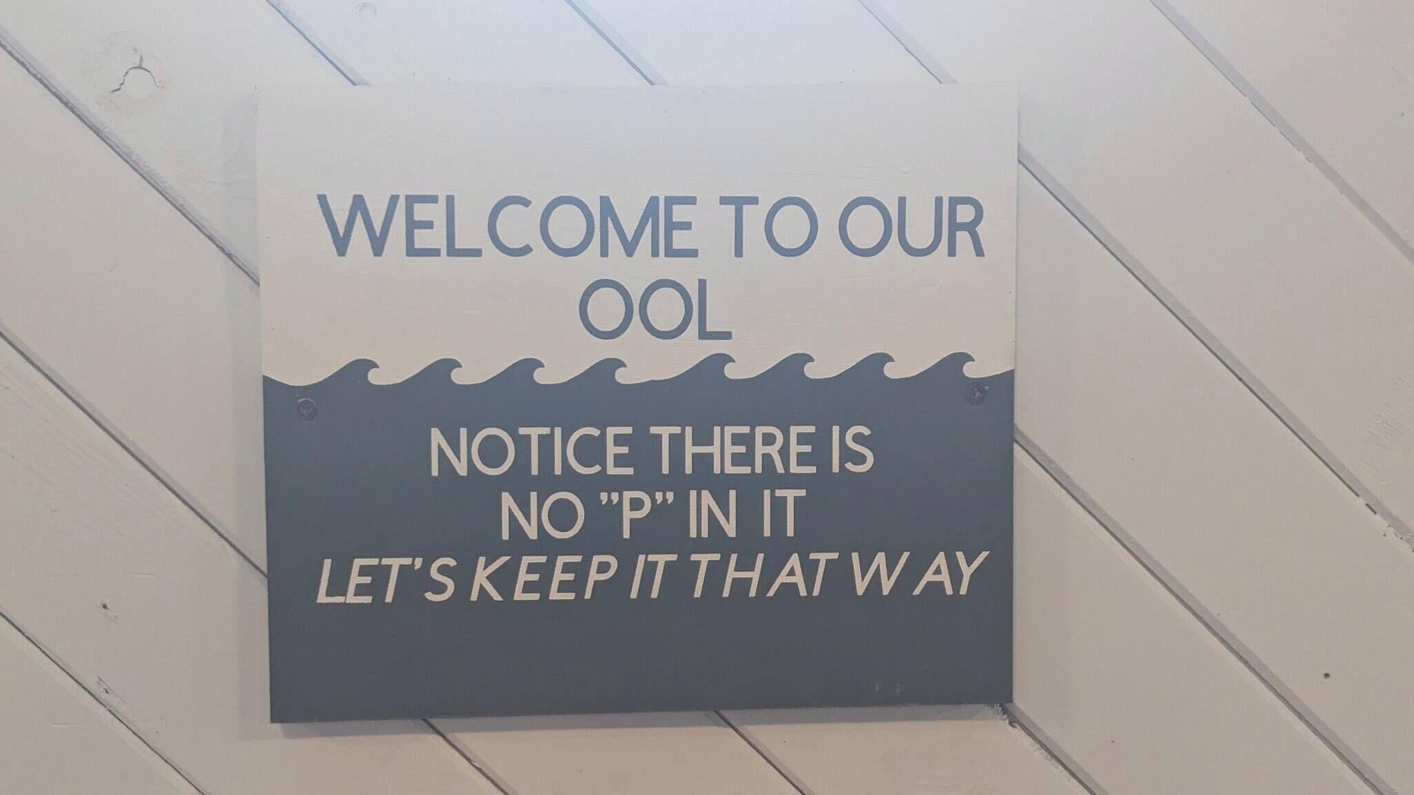 A sign with the text 'WELCOME TO OUR OOL' and 'NOTICE THERE IS NO 'P' IN IT LET'S KEEP IT THAT WAY'.