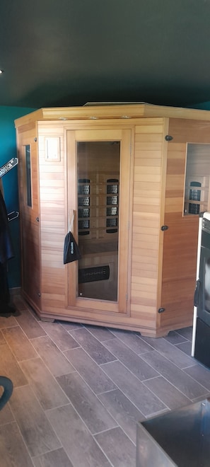 A wooden sauna with a glass door, a small shelf, and a bag hanging on the door.