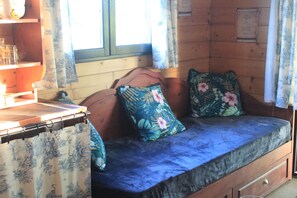 A wooden cabin interior with a sofa bed, a small table, and a window with curtains.