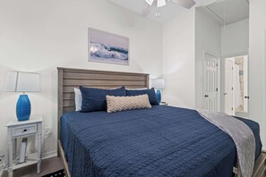 A bedroom with a bed, two bedside tables, a nightstand, a wall-mounted picture, and a door.