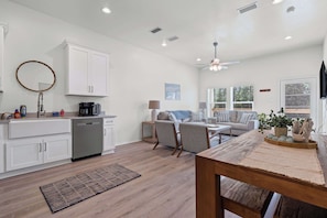 A modern kitchen with white cabinets, a dishwasher, and a dining area with a wooden table and chairs.