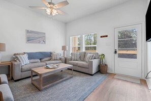A modern living room with two sofas, a coffee table, a ceiling fan, and a door with a window.