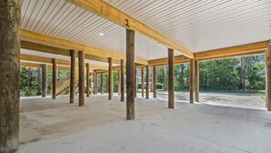 An open interior space with wooden beams and columns, a concrete floor, and a view of the outdoors. - Luxury Retreat on Oleander - Unit I (Dauphin Island)