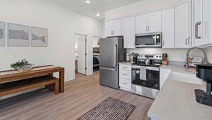 A modern kitchen with white cabinets, stainless steel appliances, and a wooden bench. - Luxury Retreat on Oleander - Unit I (Dauphin Island)